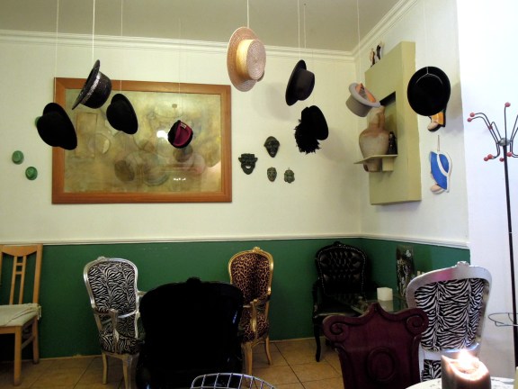 Back room of Qupi cafe, with vintage hats hanging from the ceiling, and mismatched chairs upholstered in leopard print