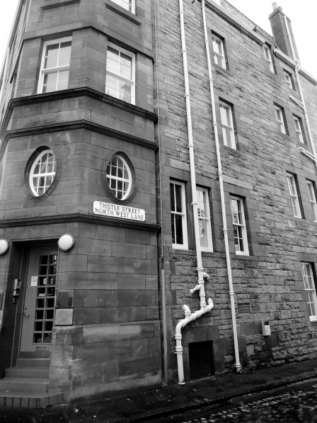 B/W photo of side of brick building with sign reading "Thistle Street North West Lane"