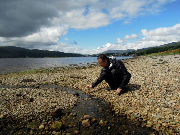 Erik squatting by a little stream on the beach at Caol waterfront