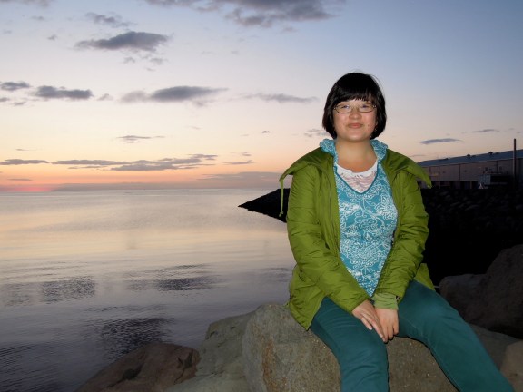 Sitting at a different end of the harbor than where "Sun Voyager" is; this side is still beautiful but feels more industrial and had many little bugs flying around. Lisa on a rock by the harbor at sunset