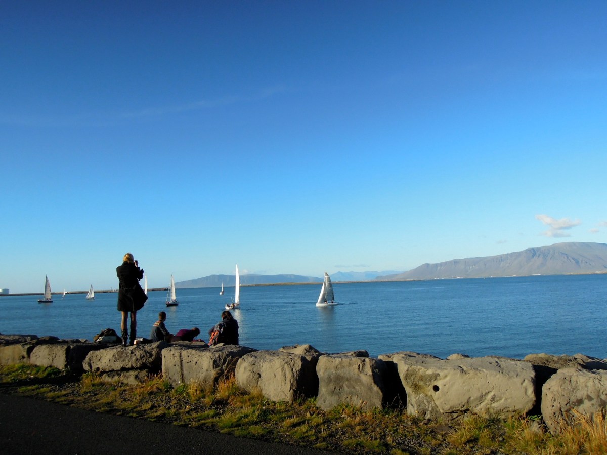 People sitting on the rocks and a girl standing and taking a picture