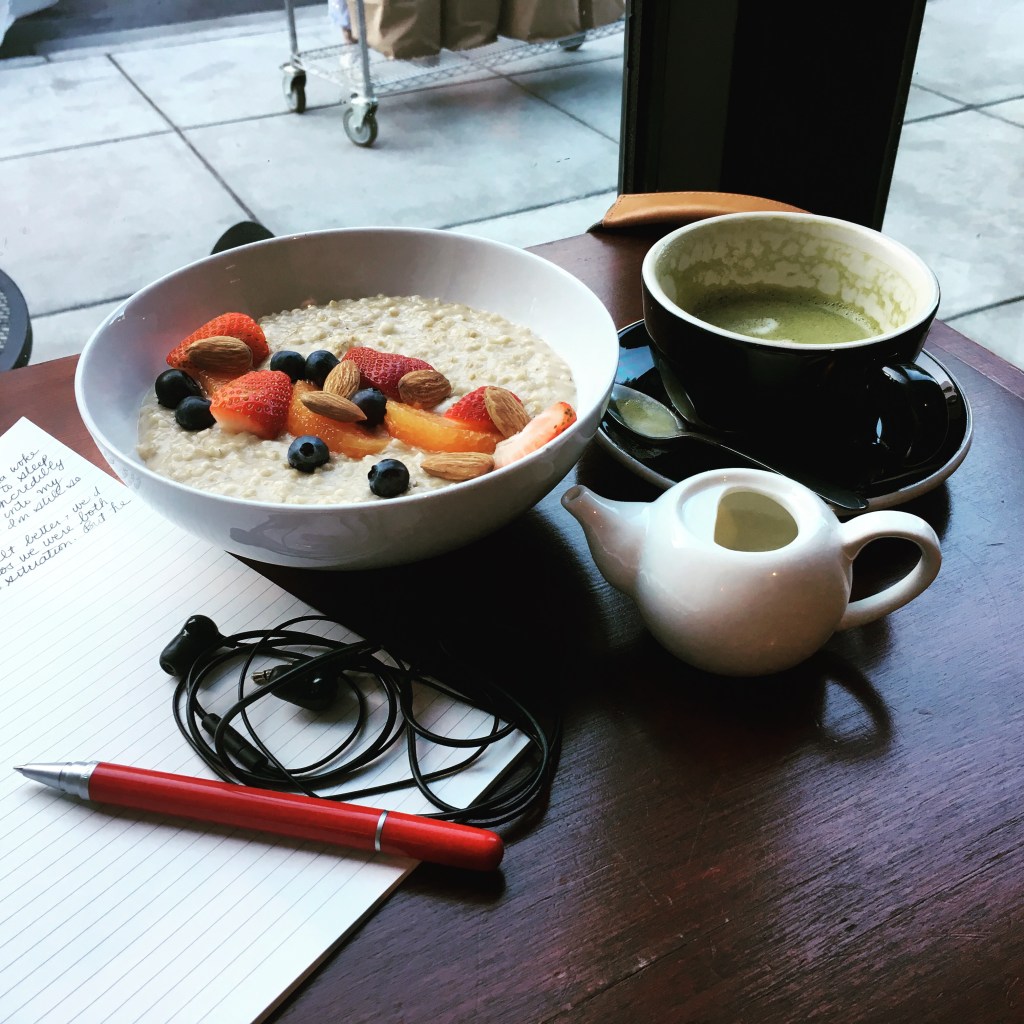 Matcha latte, oatmeal with fruit, earbuds, pen, journal