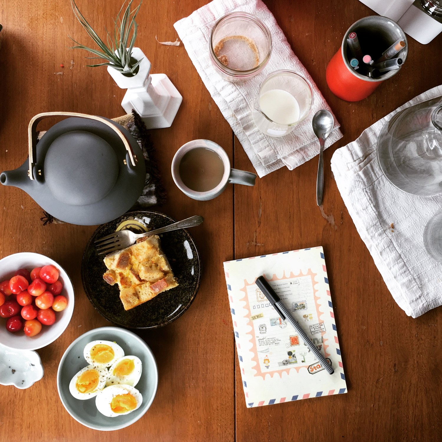 Aerial view of a journal and pen surrounded by tea service and breakfast items