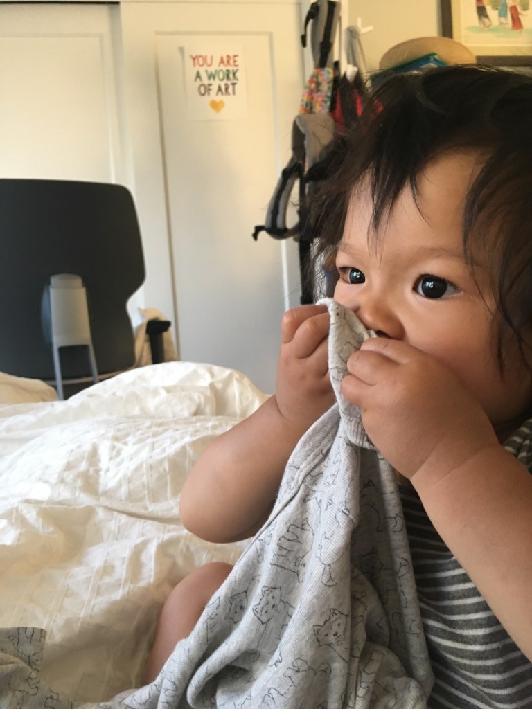 16-month-old Ada holding a onesie to her face