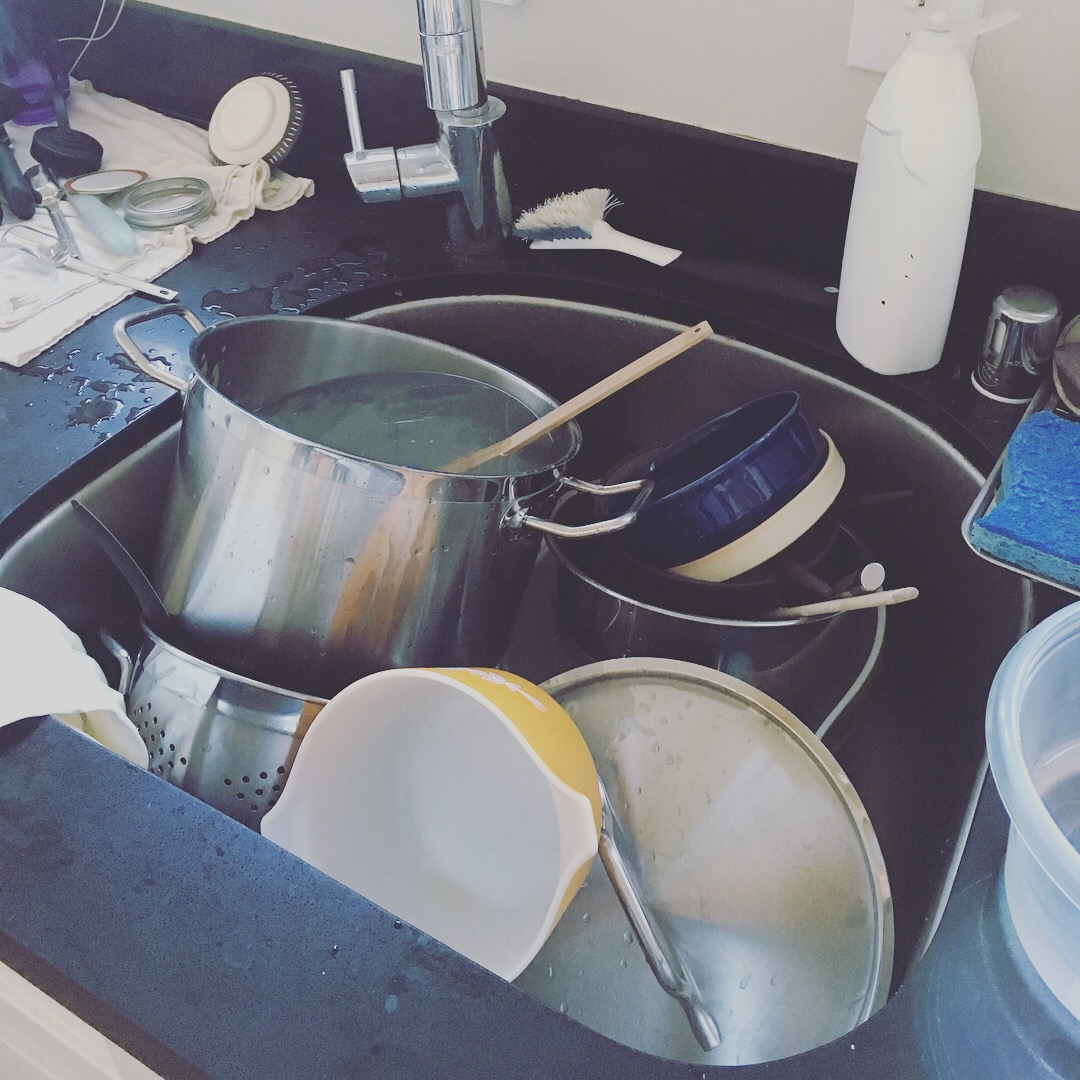A deep stainless-steel sink filled up with dirty dishes and pots