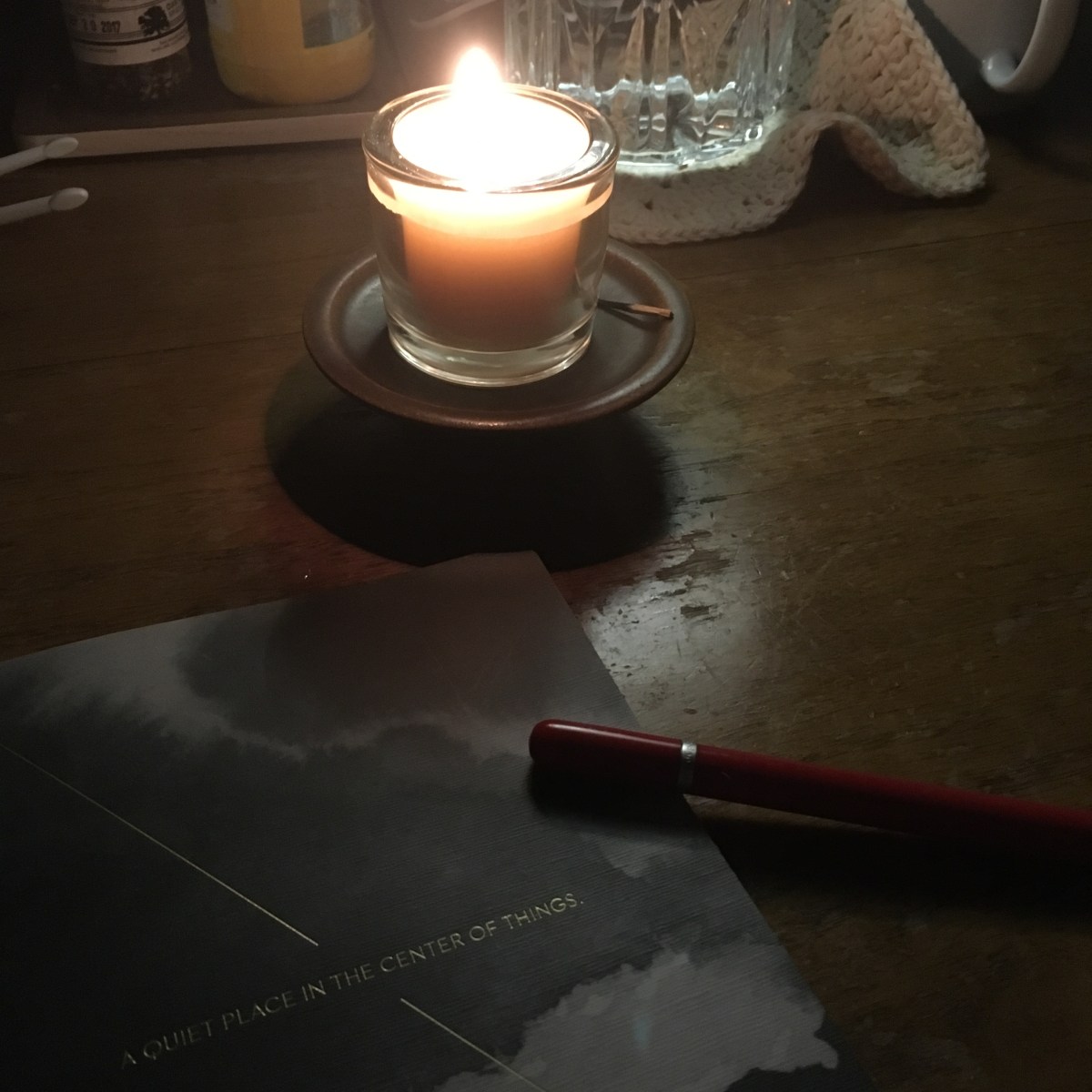 A lit candle at night, with a journal and pen nearby