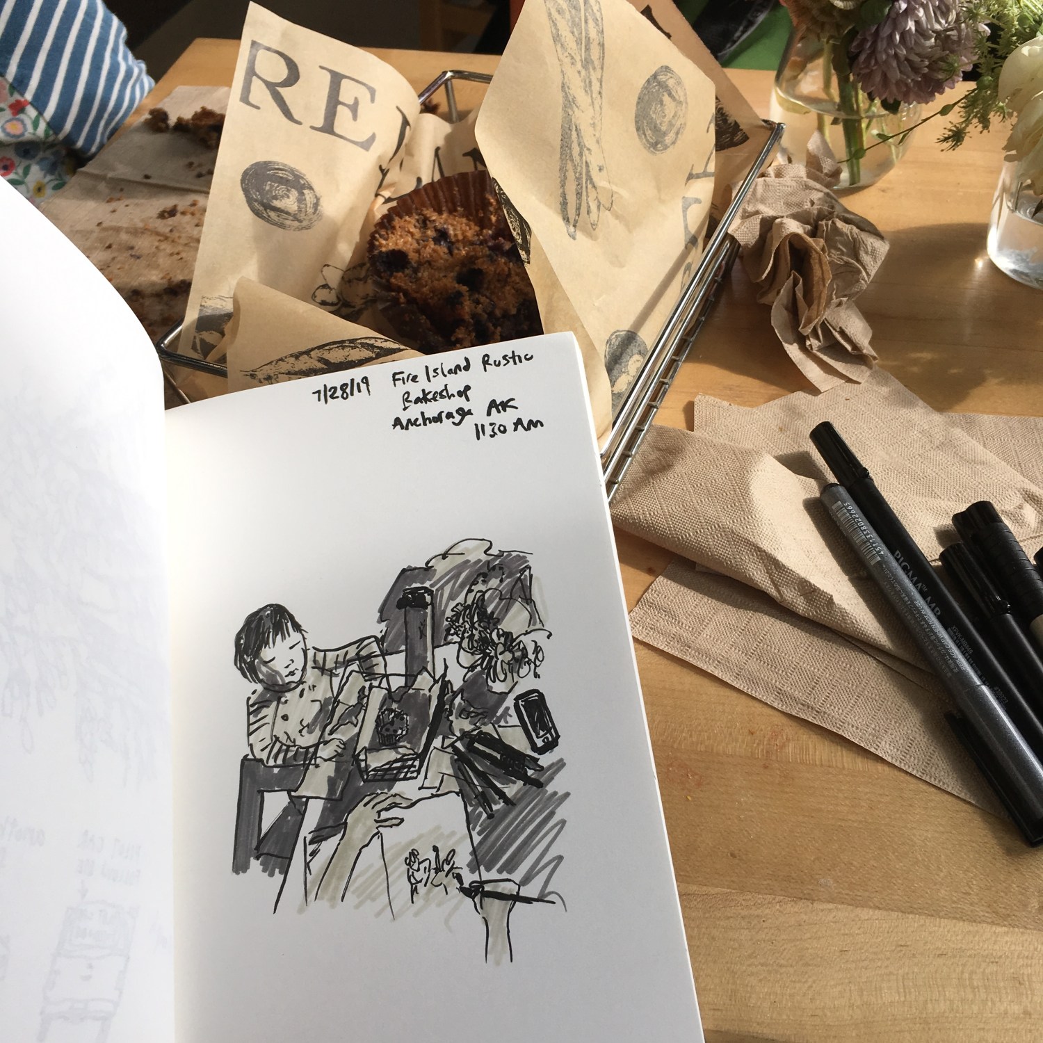 Greyscale ink sketch of a toddler in a sketchbook on a cafe table