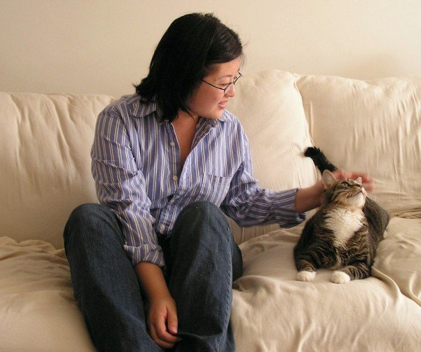 Asian woman in blue striped button-down shirt and jeans, petting a grey tabby cat