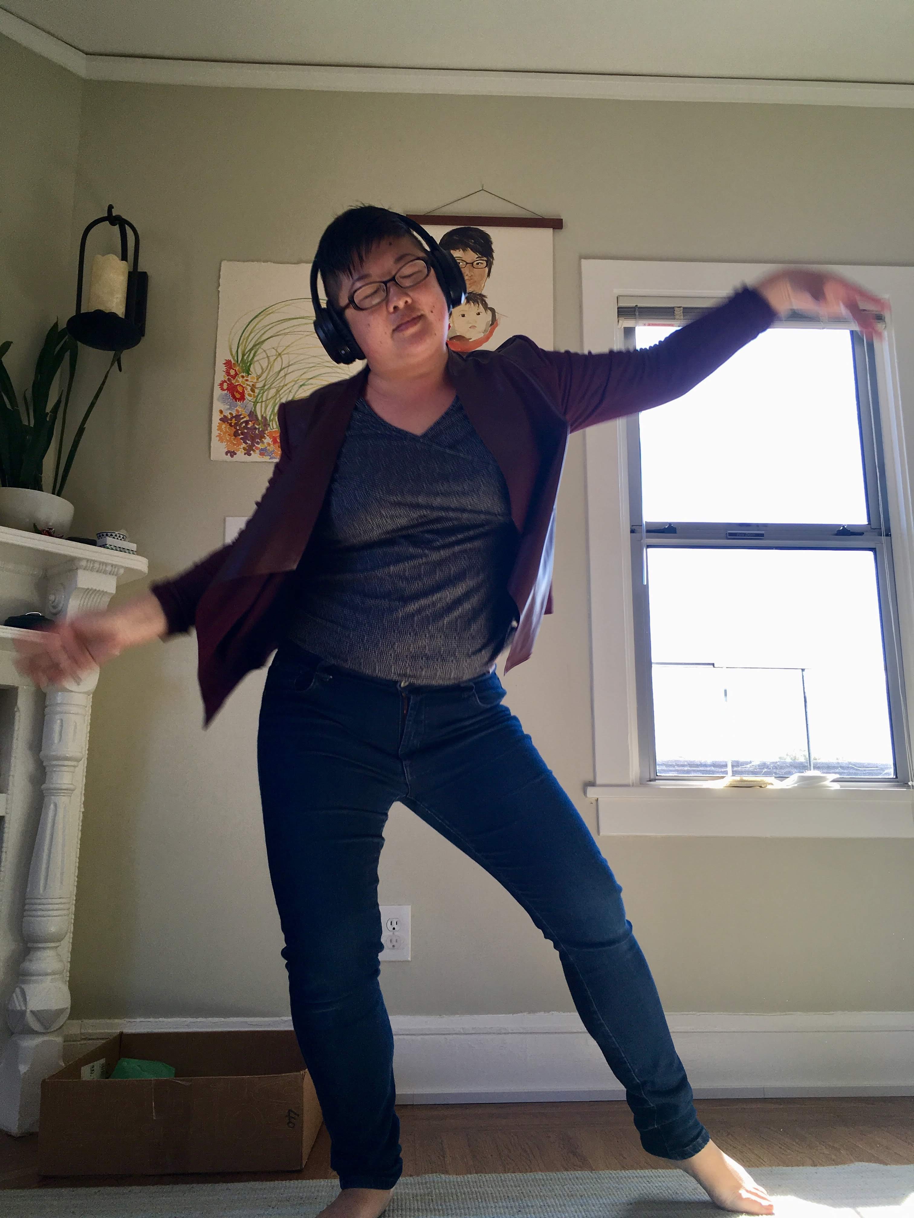 Short-haired, glasses-and-headphones-wearing Asian woman dances indoors