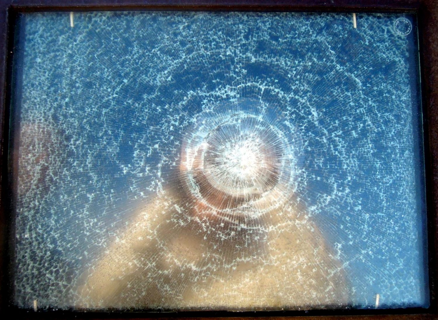 A light-skinned person takes a mirror selfie in a pane of glass so shattered their face is obscured