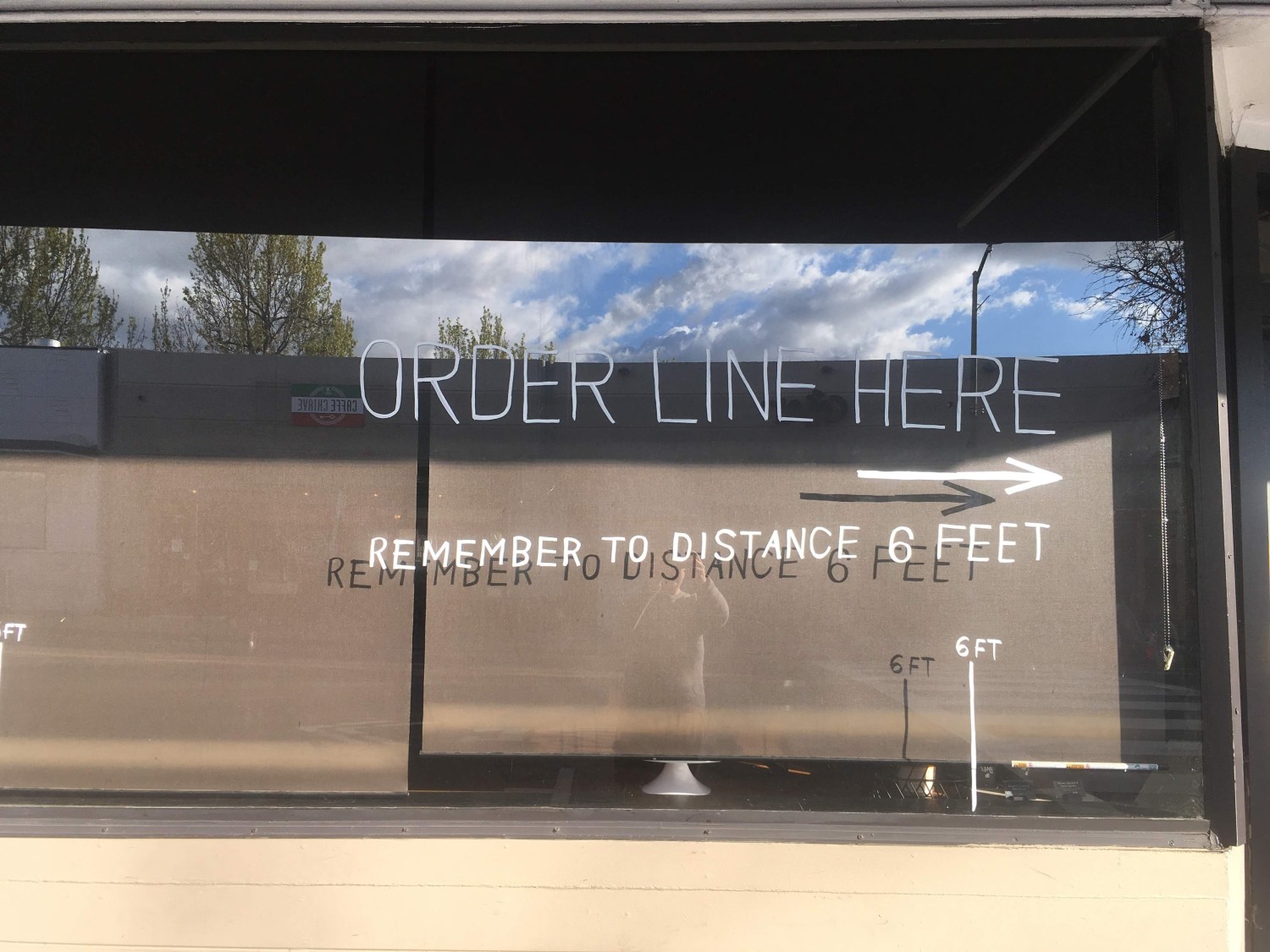 Words painted on a store window requesting customers to socially distance while in line