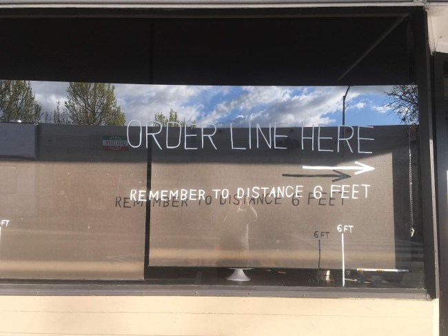 Words painted on a store window requesting customers to socially distance while in line