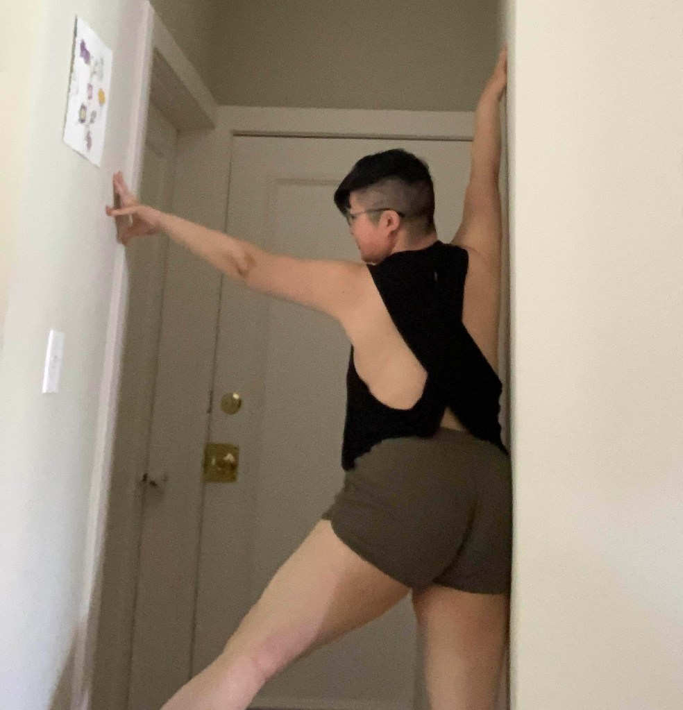 Short-haired person wearing a minimal black top and olive short shorts