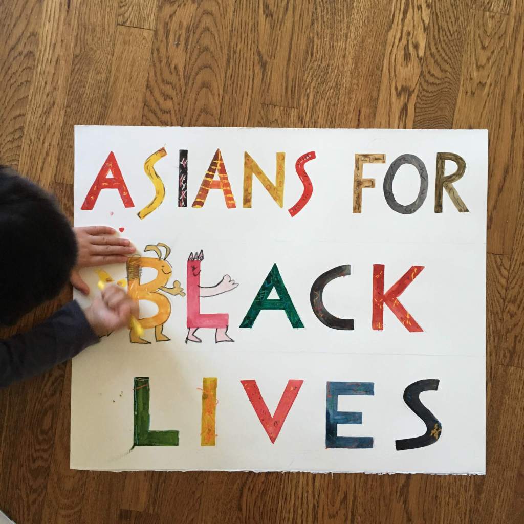 Dark-haired 4yo coloring an ASIANS FOR BLACK LIVES hand-painted sign