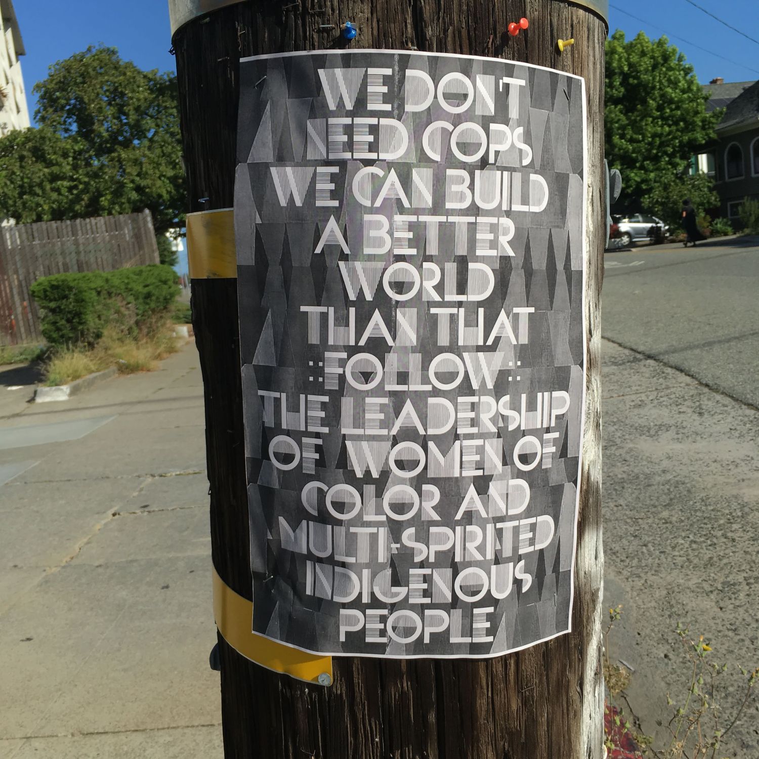 Greyscale flyer on a phone pole: We don't need cops / We can build a better world than that / Follow the leadership of women of color and multi-spirited indigenous people