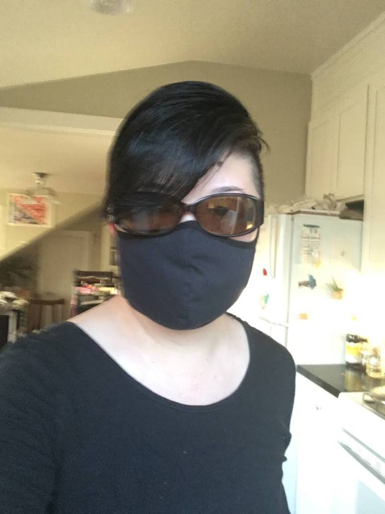 Short-haired Asian person in sunglasses and black mask, looking into the camera.