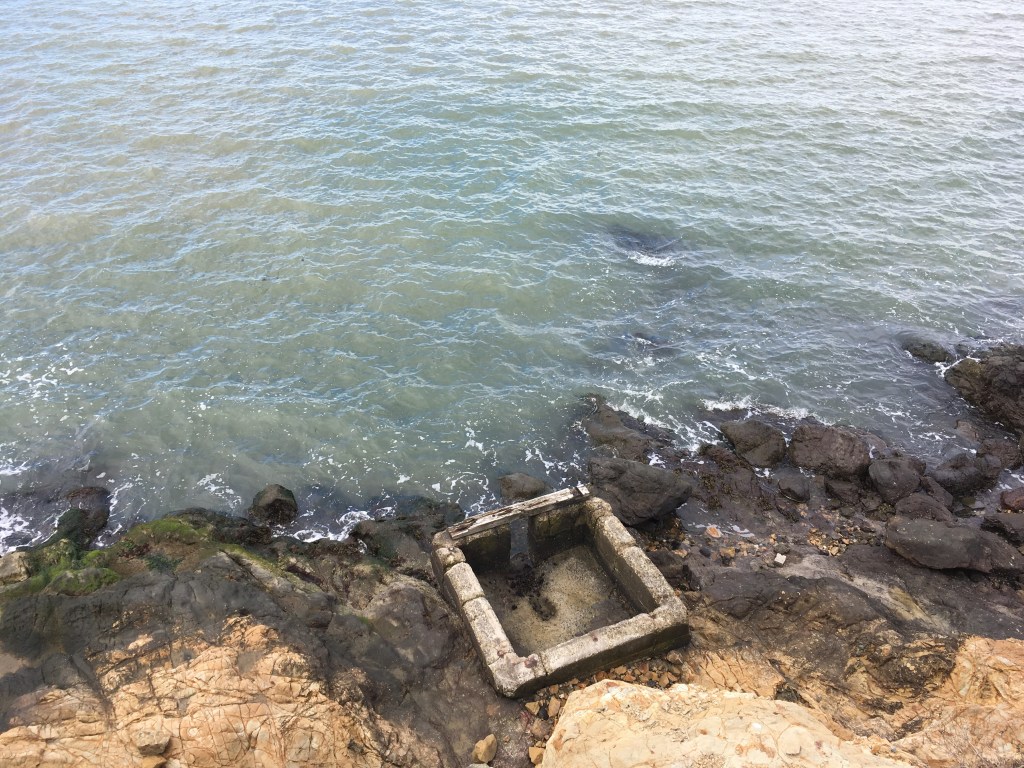 Aerial view of an abandoned, roofless structure on a rocky shoreline