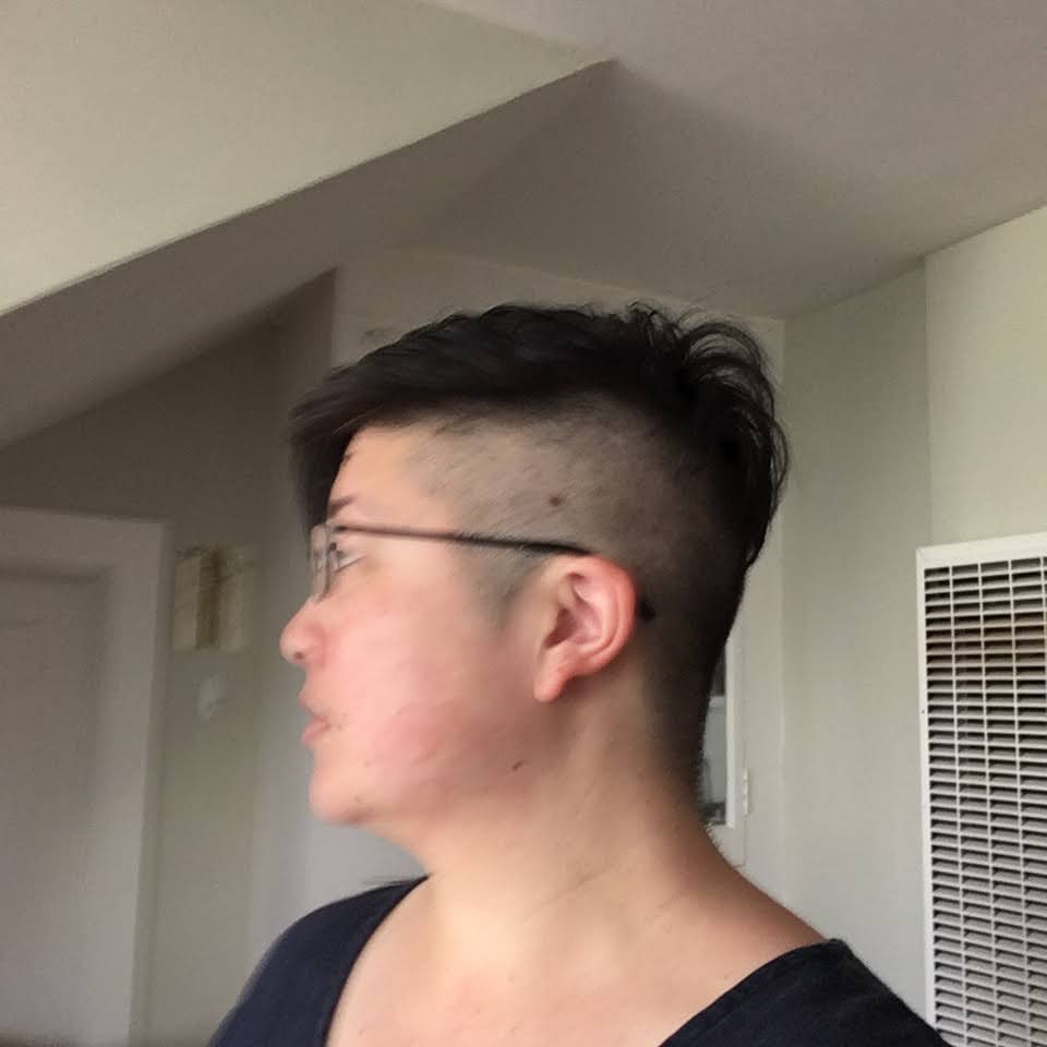 Asian person in profile with short hair and shaved side, wearing glasses