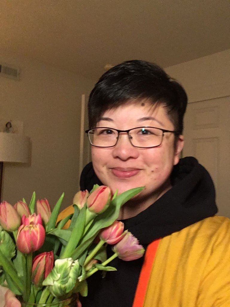 Lisa Hsia, a short-haired East Asian person with glasses, smiles while holding a bouquet of tulips.