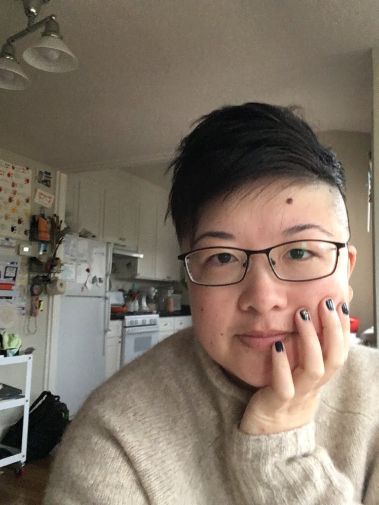 Lisa Hsia, a short-haired Asian person with glasses, shows very dark painted nails